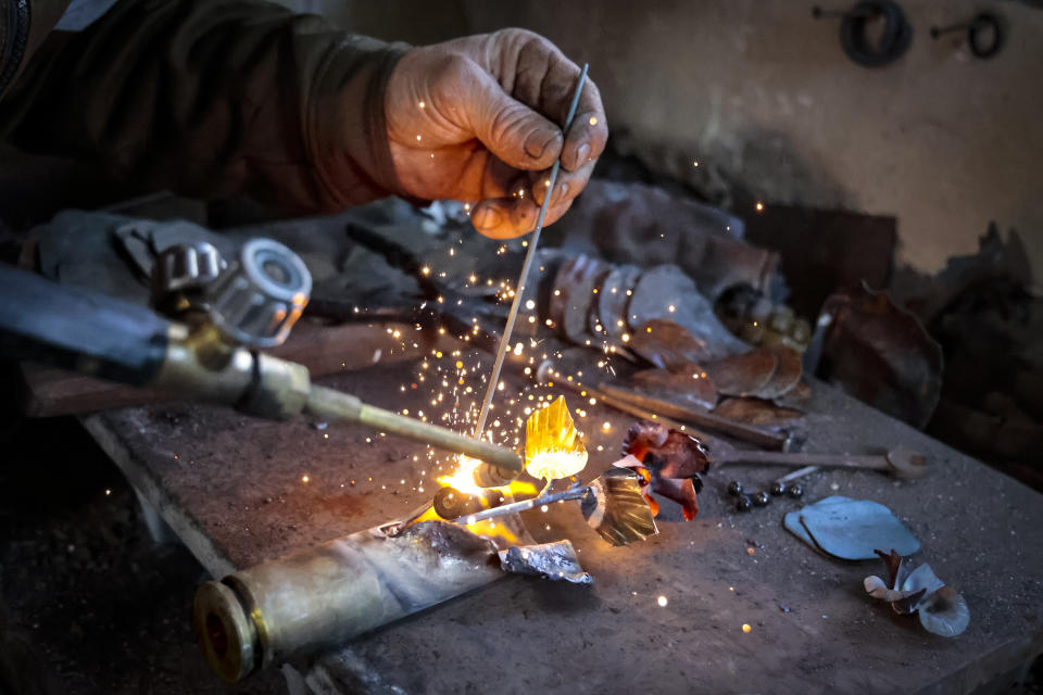 Viktor Mikhalev works in a workshop in his house in Donetsk, Russian-controlled Donetsk region, eastern Ukraine, Saturday, March 4, 2023. Mikhalev is transforming weapons and ammunition into flowers of war. Mikhalev, trained as a welder, lives and works in a house whose fence and door are decorated with forged flowers and grapes. (AP Photo/Alexei Alexandrov)