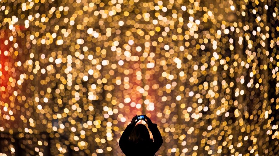 Eine Frau fotografiert die Fassade eines mit Lichterketten weihnachtlich geschmückten Einkaufszentrums.