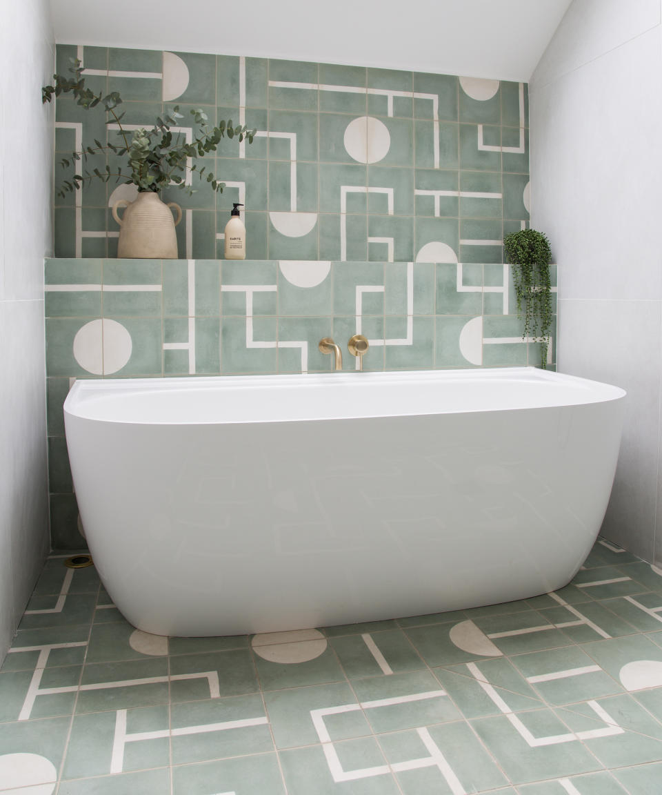 Green and white tiles from the floor that run up on to the accent wall behind the bath