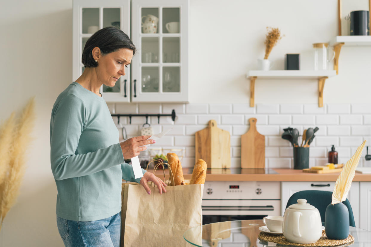 Senior female frustrated while looking at receipt from grocery store. Rise in price of products concept. Buying consumer goods during inflation. Wisely planning family budget and managing expenses. Facing economic downturn, copy space