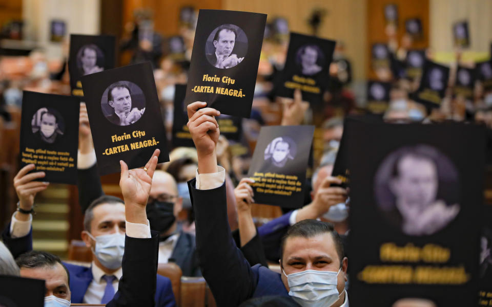 Opposition members of parliament hold leaflets showing prime minister-designate Florin Citu, reading "The Black Book" during a session called to vote on the government team in Bucharest, Romania, Wednesday, Dec. 23, 2020. Romania's president Klaus Iohannis appointed on Tuesday, the outgoing finance minister as prime minister-designate after three pro-Western center-right groups joined forces to keep out of power a left-leaning populist party that won most votes at a parliamentary election earlier this month. (AP Photo/Vadim Ghirda)