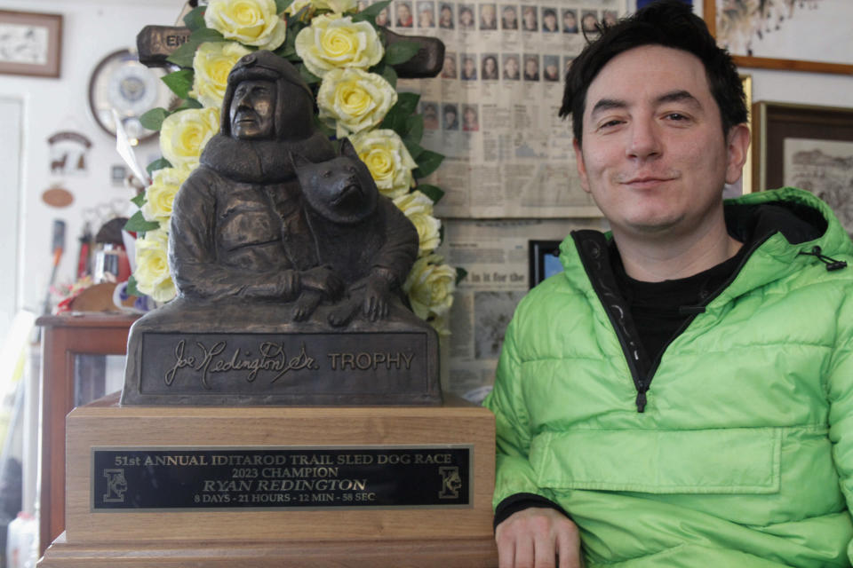 Ryan Redington, the 2023 Iditarod Trail Sled Dog champion, poses with his trophy Monday, Feb. 26, 2024, in Knik, Alaska. The trophy features a likeness of his grandfather Joe Redington Sr., a co-founder of the world's most famous sled dog race. (AP Photo/Mark Thiessen)