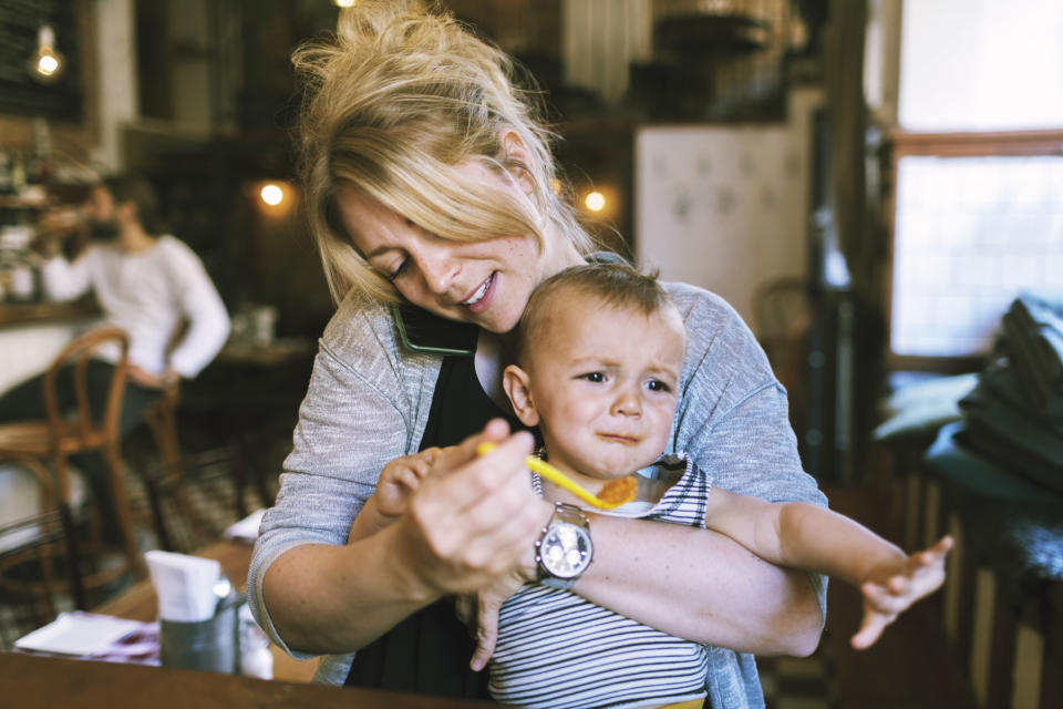 Woman feeding a baby in a highchair while on the phone