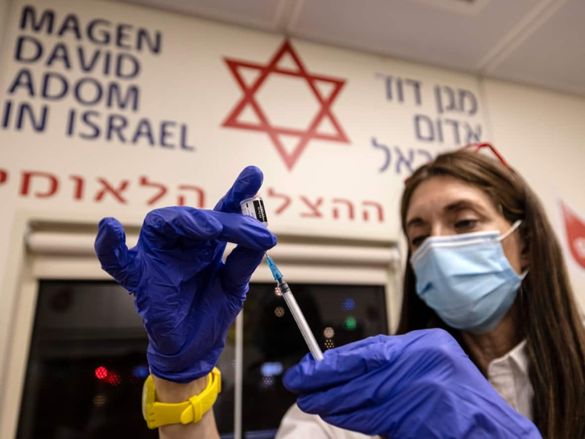 A medic from Israel's Magen David Adom emergency service prepares a booster shot of the coronavirus vaccine in Tel Aviv in August. The recommendation by an Israeli panel to administer a fourth vaccine to those who are over 60 is being met with a tepid response by some of the country's medical experts, who believe more data is needed.   (Tsafrir Abayov/The Associated Press - image credit)