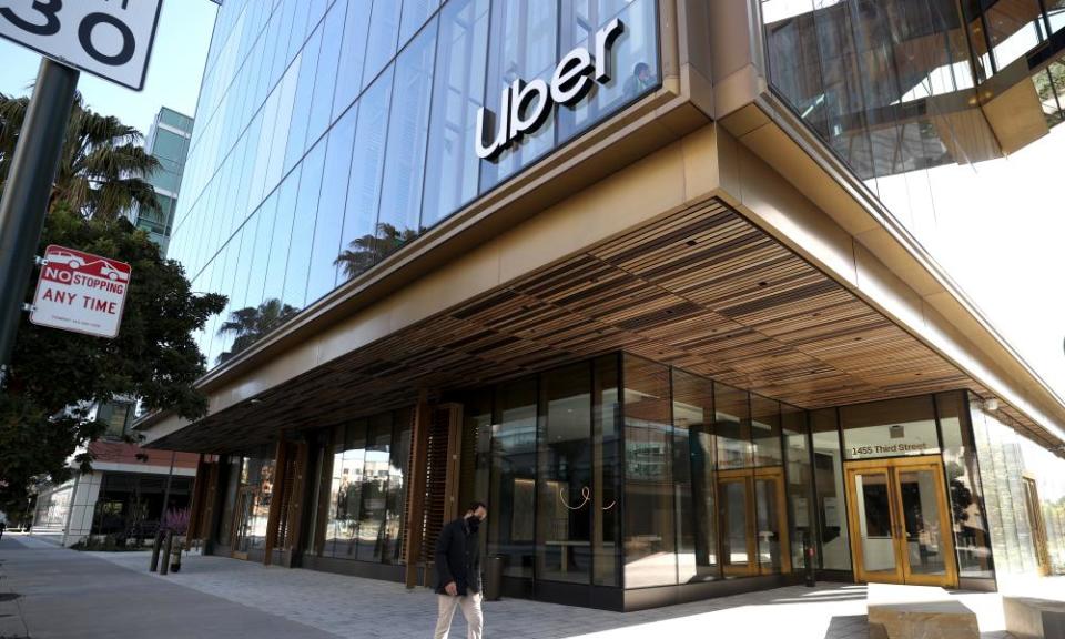 A glass and steel building with a large overhang above the ground floor, and the Uber logo on its corner