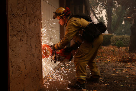 A Cal Fire firefighter uses a saw to gain access to a burning structure while battling the Camp Fire in Paradise, California, U.S., November 9, 2018. REUTERS/Stephen Lam