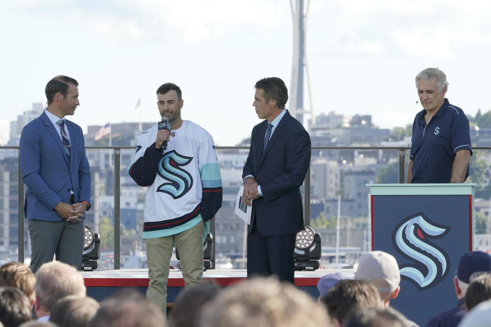 Jordan Eberle, second from left, a forward from the New York Islanders, is introduced as a new player for the Seattle Kraken as he stands with ESPN NHL hockey draft hosts Dominic Moore, left, and Chris Fowler, second from right, Wednesday, July 21, 2021, as Kraken general manager Ron Francis, right, listens during the Kraken's NHL hockey expansion draft event in Seattle. (AP Photo/Ted S. Warren)