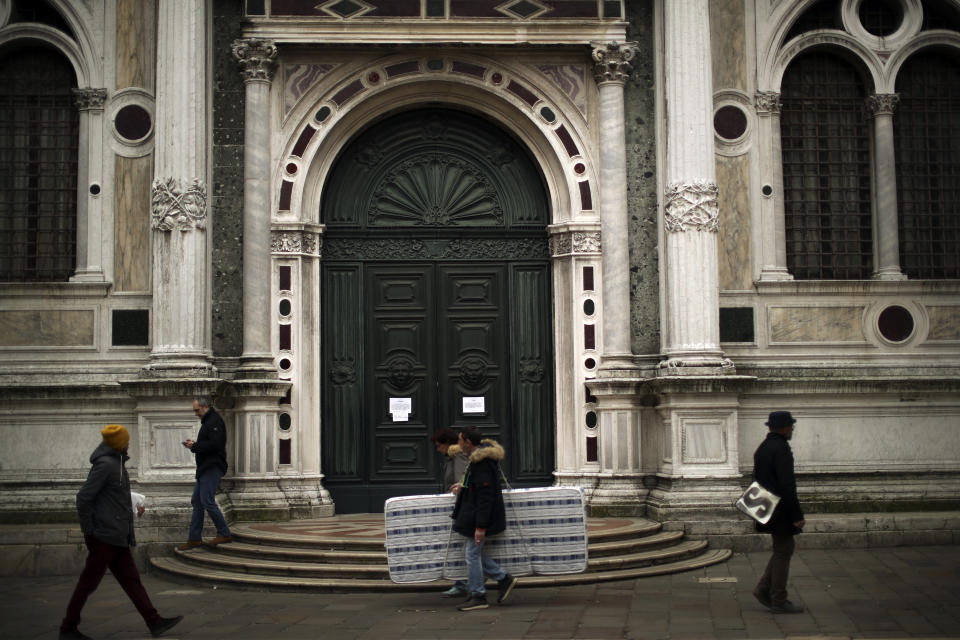People walk past St Roch church, temporary closed due to the COVID-19 virus outbreak, in Venice, Saturday, Feb. 29, 2020. A U.S. government advisory urging Americans to reconsider travel to Italy due to the spread of a new virus is the "final blow" to the nation's tourism industry, the head of Italy's hotel federation said Saturday. Venice, which was nearing recovery in the Carnival season following a tourist lull after record flooding in November, saw bookings drop immediately after regional officials canceled the final two days of celebrations this week, unprecedented in modern times. (AP Photo/Francisco Seco)