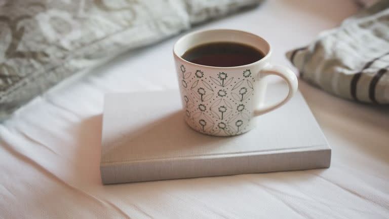 book and cup of black coffee on a bed