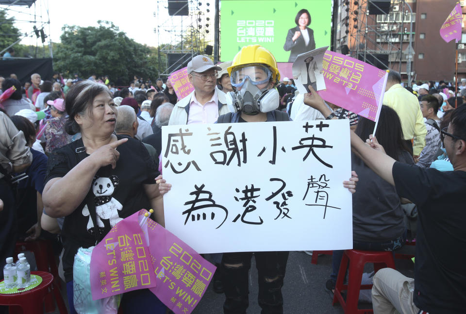 A hong Kong supporter of Taiwan President and Democratic Progressive Party presidential candidate Tsai Ing-wen, holds a slogan reading "Thanks to President Tsai, Statement for Hong Kong", as Tsai seen in poster behind launches her re-election campaign in Taipei, Taiwan, Sunday, Nov. 17, 2019. Taiwan will hold its presidential election on Jan. 11, 2020. (AP Photo/Chiang Ying-ying)