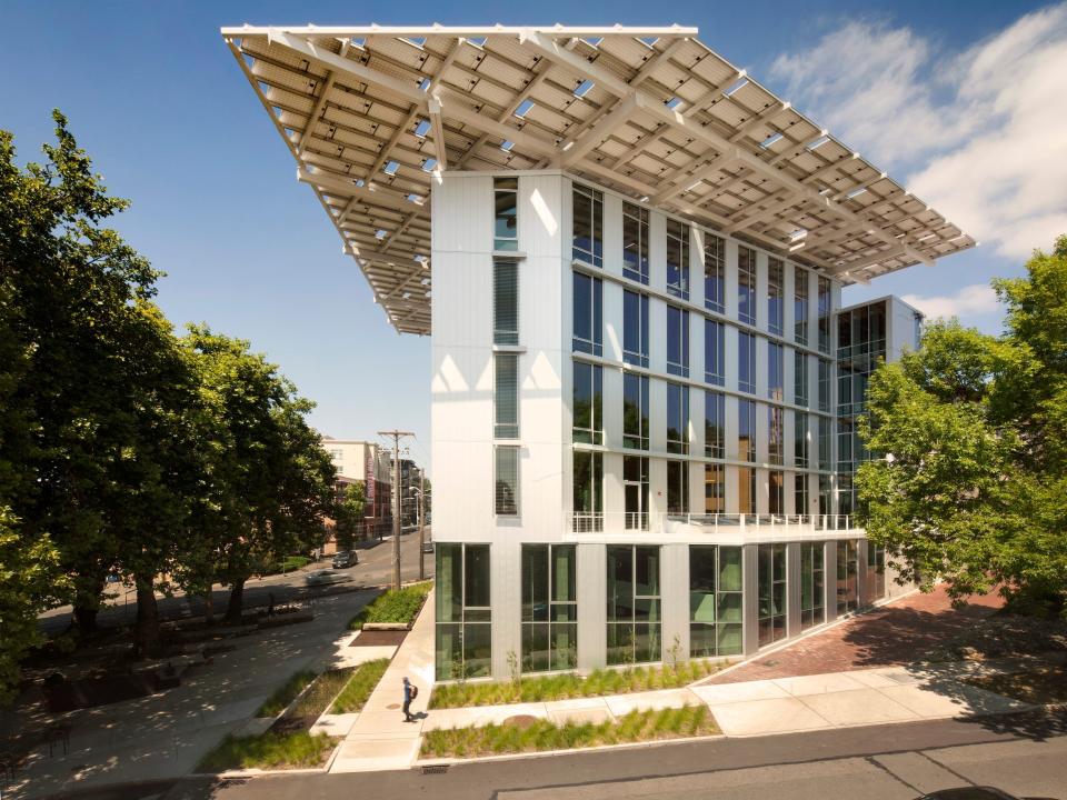 A photo of the exterior of the Bullitt Center in Seattle, Washington. The building is tall and thin with many windows and has a large canopy on top.