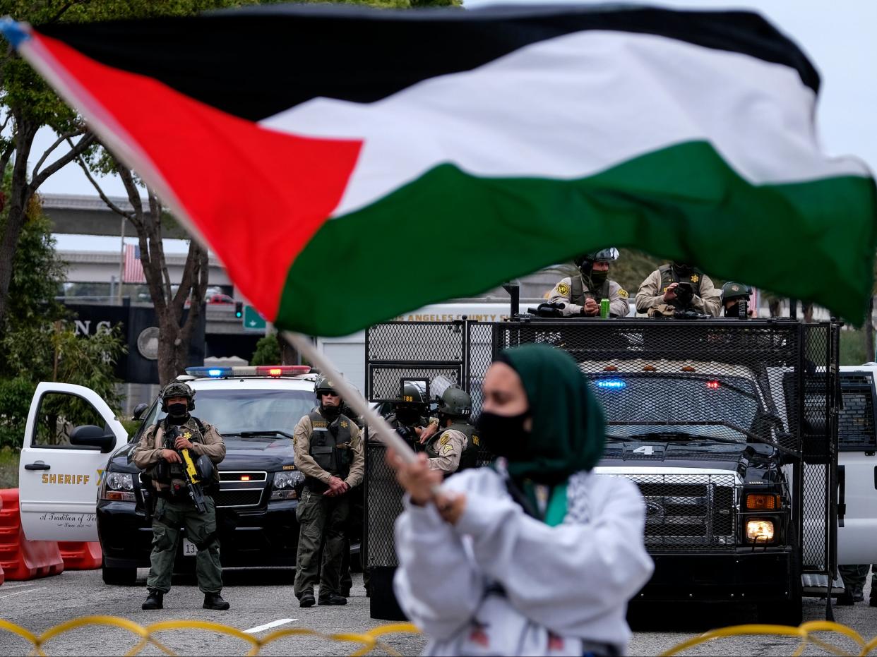 A demonstrator waves the flag of Palestine as police officers guard outside the Federal Building during a protest against Israel and in support of Palestinians in the Westwood section of Los Angeles on Saturday (AP)