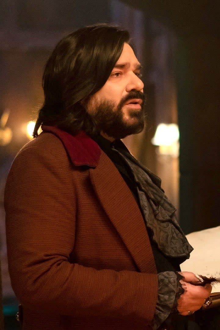 Two men, dressed in period clothing, stand in a dimly lit room with candles. They appear to be discussing something. (Characters from What We Do in the Shadows)