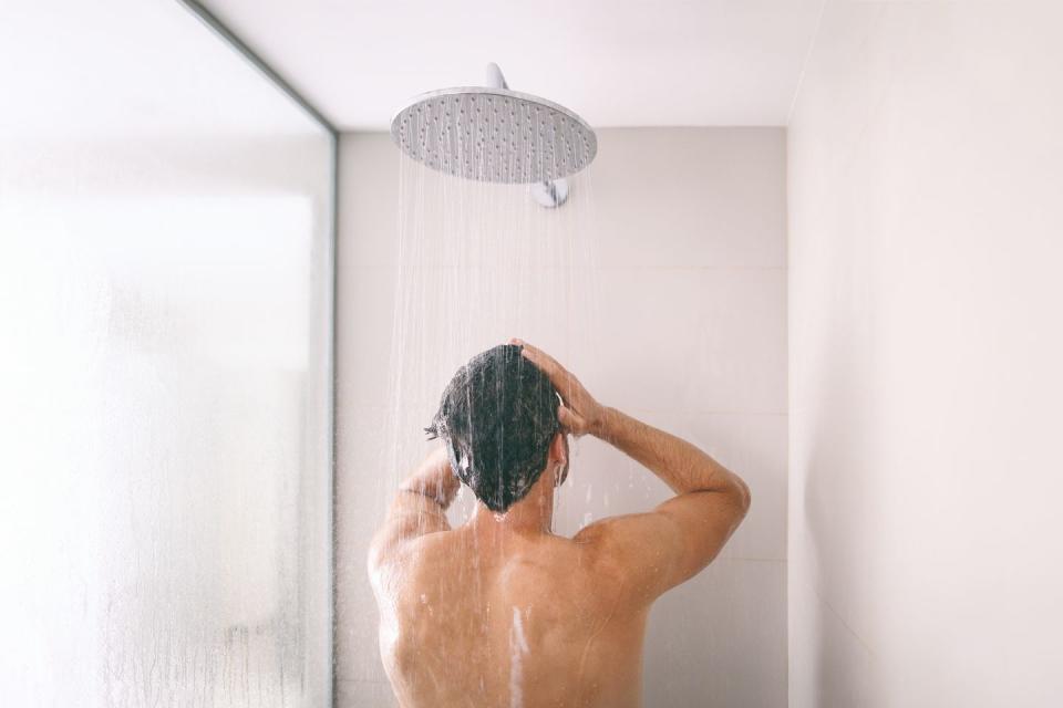 man taking a shower washing hair with shampoo product under water falling from luxury rain shower head morning routine luxury hotel lifestyle guy showering body care hygiene