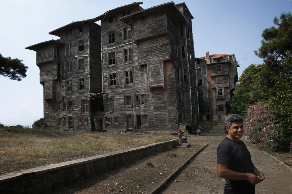 In this Saturday, July 21, 2018 photo, Erol Baytas, 56, the caretaker of the 6-floor timber building that once served as an orphanage for children of the minority Greek community, stands on its grounds, in Buyukada, the largest and most popular of the Princes' Islands in the Sea of Marmara near Istanbul. The 120-year-old gigantic Prinkipo orphanage, occupying 20,000 square meters on a hilltop became home for some 5,800 minority Greek children from 1903 until 1964 when it was forced to shut down. (AP Photo/Lefteris Pitarakis)