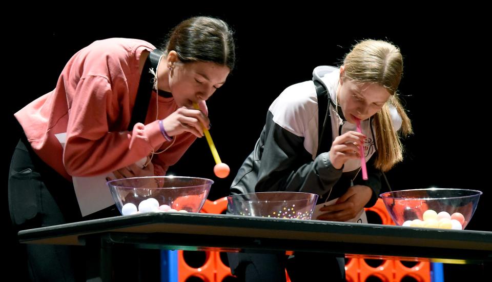 Bedford High School sophomores Kaitlyn Kwiatkowski and Cheyenne Ivey take part in a "check your lungs" game by sucking up ping pong balls through a straw and then placing them in the bowl. The purpose was to show how substances can affect motor skills.