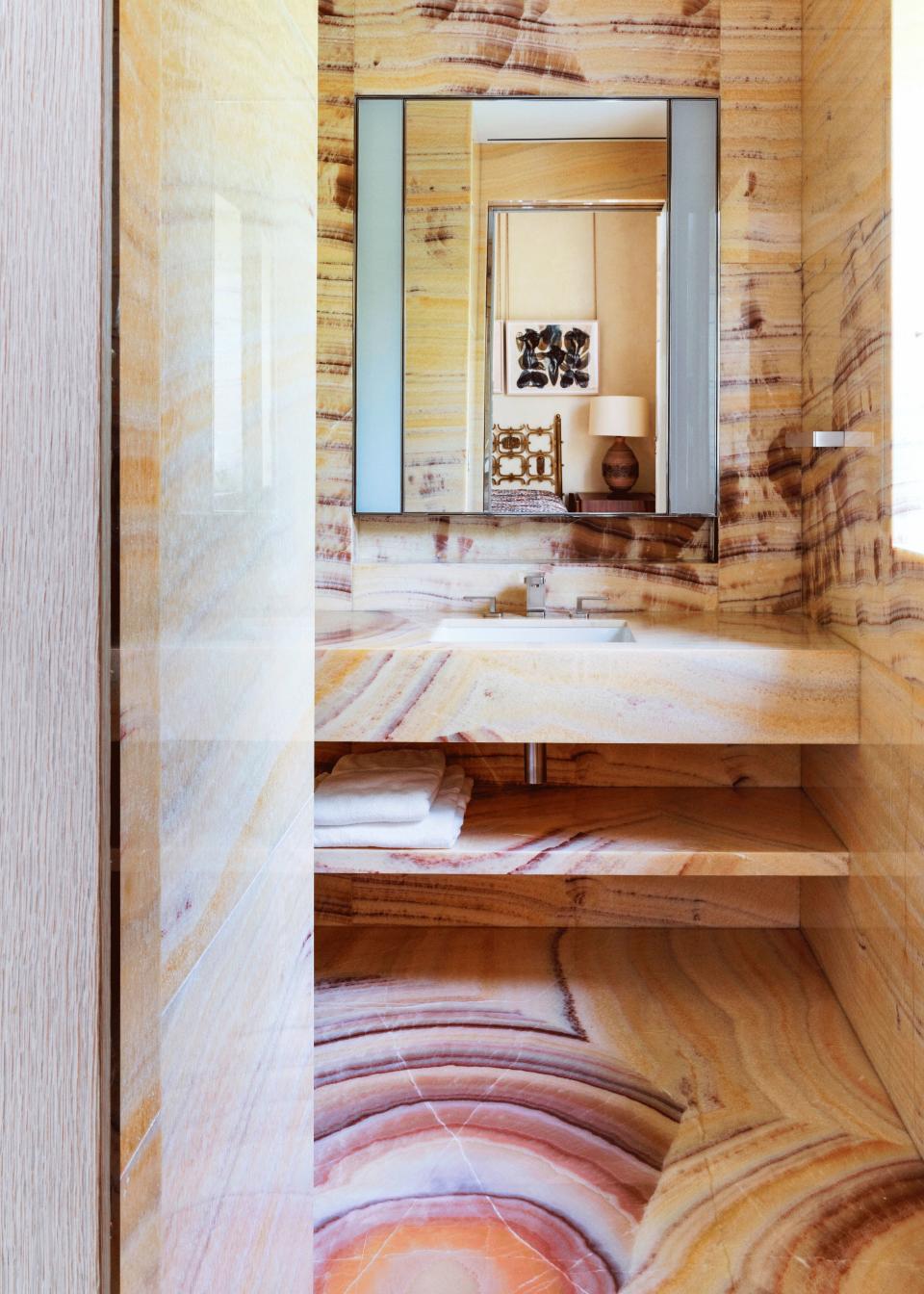 In the guest bath, the floors, wall, and vanity are made of Onyx Arco Iris. The sink, fittings, and mirrored medicine cabinet with lighting are custom-designed by Peter Marino Architect.