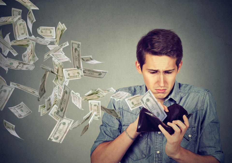 A young man grimaces as dollar bills fly out of his wallet.