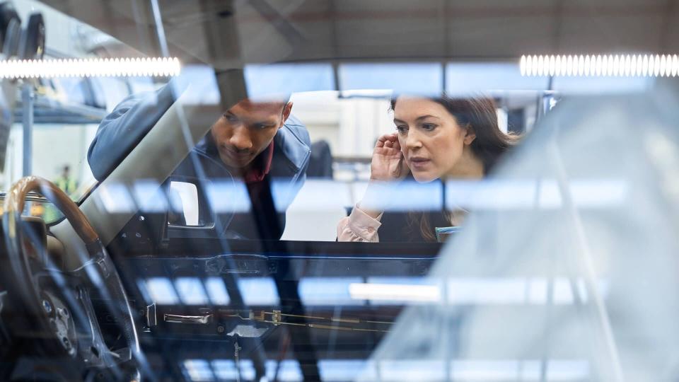 Engineer and manager looking inside car seen through window.