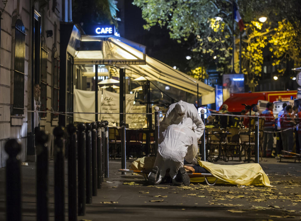 FILE - In this Nov.13, 2015 file photo, investigating police officers inspect the lifeless body of a victim of a shooting attack outside the Bataclan concert hall in Paris. France is commemorating the fourth anniversary of the Islamic State attacks in Paris. The attacks on Nov. 13, 2015, left 131 people dead at the country's national stadium, the Bataclan concert hall and bars and restaurants in the city center. (AP Photo/Kamil Zihnioglu, File)