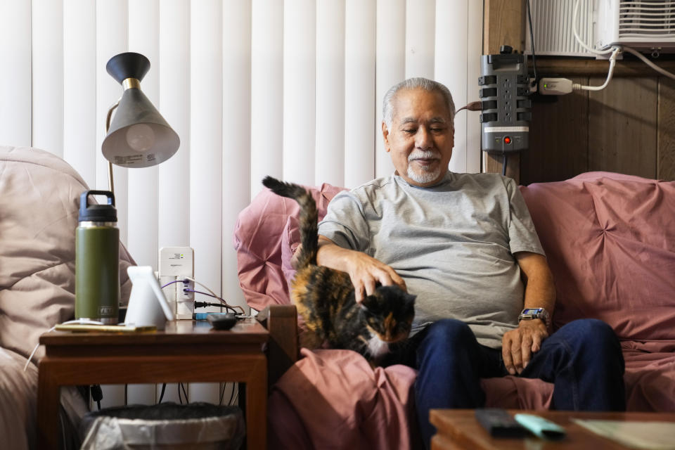 Weslee Chinen, whose wife Sharlene Rabang was named as the 100th victim of the Lahaina wildfires after dying weeks after fleeing their home, pets Sharlene's adopted cat Poke, who was rescued from the fires, Tuesday, Dec. 5, 2023, at his family home in Waipahu, Hawaii. Rabang, who had a previous history of cancer, COVID and high blood pressure, was not originally listed as a victim until her family fought to have her included, citing smoke inhalation as a contributing factor. Chinen was in Oahu at the time of the fires, and Rabang's son Brandon had to convince her to flee. (AP Photo/Lindsey Wasson)