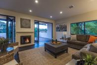 <p>The home’s focal point is its open-concept living and dining room. The living room has large, folding glass doors, which open up to a raised patio, and a fireplace. (Zillow) </p>