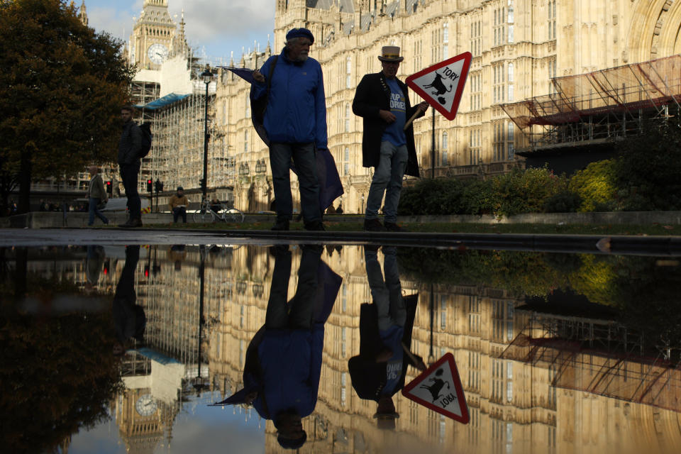 Protestors are reflected in a puddle opposite parliament after Britain's Prime Minister Liz Truss resigned in London, Thursday, Oct. 20, 2022. Truss resigned Thursday, bowing to the inevitable after a tumultuous, short-lived term in which her policies triggered turmoil in financial markets and a rebellion in her party that obliterated her authority.(AP Photo/David Cliff)
