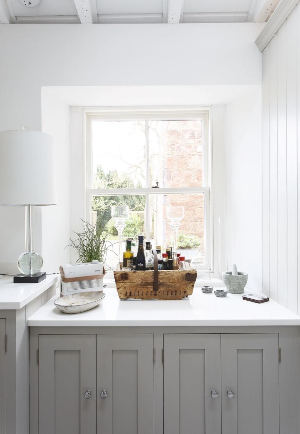 White and gray kitchen with pale gray Shaker style units, white walls and windows.