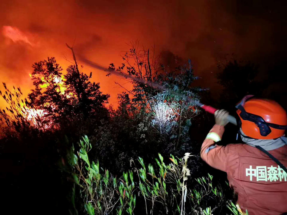 In this Monday, March 30, 2020 photo, a firefighter battles a forest fire as it approaches a gas station in Xichang in southwestern China's Sichuan Province. More than a dozen of people have died while fighting a raging forest fire in southwestern China and reinforcements were sent to fight the blaze and evacuate nearby residents, officials and state media reported Tuesday. (Chinatopix via AP)