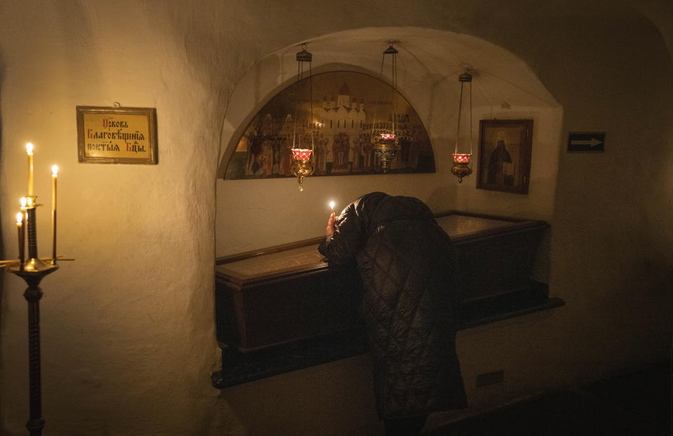 A believer holds a candle as she prays at a sarcophagus with holy relics in the underground labyrinth of the Monastery of the Caves, also known as Kyiv-Pechersk Lavra, one of the holiest sites of Eastern Orthodox Christians, in Kyiv, Ukraine, Friday, March 24, 2023. Tensions are on the rise at a prominent Orthodox monastery in Kyiv where the monks are facing eviction later this month. The Ukrainian government accuses the monks of links to Moscow, even though they claim to have severed ties with the Russian Orthodox Church following Russia's full-scale of invasion of Ukraine. (AP Photo/Efrem Lukatsky)