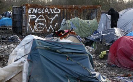 A migrant stands next to graffiti that reads "England pay now" in a muddy field at a camp of makeshift shelters for migrants and asylum-seekers from Iraq, Kurdistan, Iran and Syria, called the Grande Synthe jungle, near Dunkirk, France, January 25, 2016. REUTERS/Yves Herman