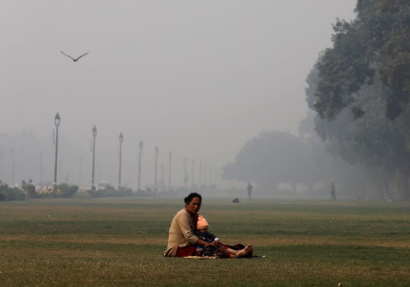 A sits with a child in a park near India Gate, on a smoggy morning, in New Delhi