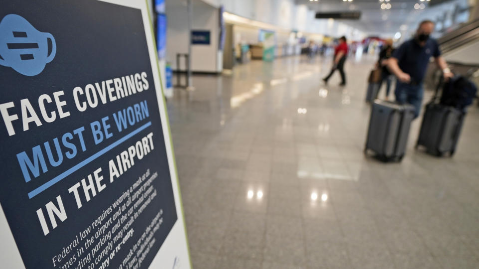 A sign requiring masks is displayed as travelers move about at Cleveland Hopkins International Airport, Wednesday, May 26, 2021, in Cleveland. (AP Photo/Tony Dejak)