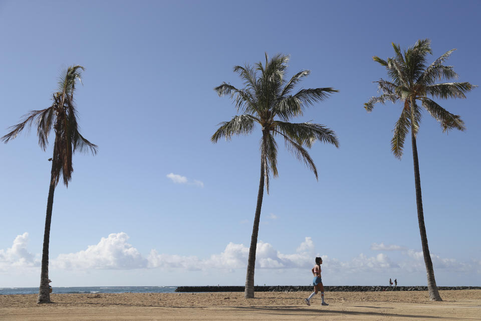 FILE - A beachgoer walks down Waikiki Beach, Thursday, Oct. 15, 2020, in Honolulu. About two years after 13 children and teens in Hawaii sued the state over the threat posed by climate change, both sides reached a settlement that includes an ambitious requirement to decarbonize Hawaii’s transportation system in the next 21 years. (AP Photo/Marco Garcia, File)