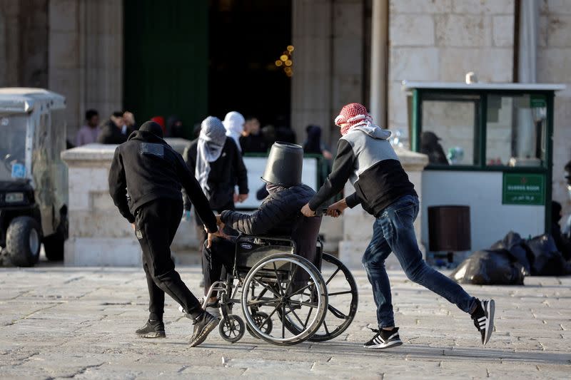 Palestinian protestors push a man on a wheel chair during clashes with Israeli security forces at the compound that houses Al-Aqsa Mosque, in Jerusalem's Old City