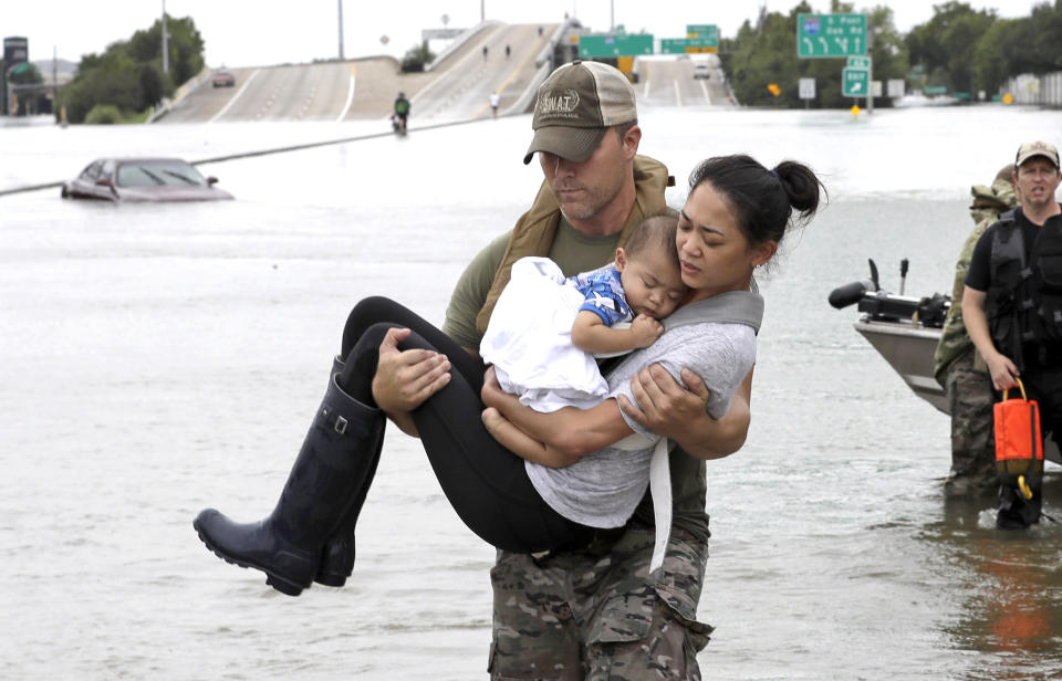 FILE - In this Aug. 27, 2017 file photo, Houston Police SWAT officer Daryl Hudeck carries Catherine Pham and her 13-month-old son Aiden, asleep in her arms, after rescuing them from their home surrounded by floodwaters from Tropical Storm Harvey in Houston, Texas. Hurricane Harvey roared onto the Texas shore nearly a year ago, but it was a slow, rainy roll that made it a monster storm. Federal statistics show some parts of the state got more than 5 feet of rain in five days. Harvey killed dozens and swamped a section of the Gulf Coast that includes Houston, the nation's fourth largest city, causing billions of dollars in damage. (AP Photo/David J. Phillip, File)