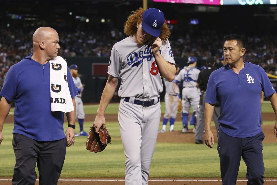 Los Angeles Dodgers relief pitcher Dustin May, middle, walks off the field as he is flanked by medical staff Neil Rampe, left, and Yosuke Nakajima, right, after May was hit by a batted ball from Arizona Diamondbacks' Jake Lamb during the fourth inning of a baseball game Sunday, Sept. 1, 2019, in Phoenix. (AP Photo/Ross D. Franklin)