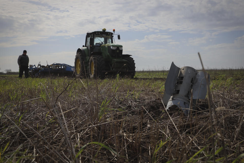 A part of a Russian rocket is seen in an agricultural field as a farmer works on a tractor during the sowing campaign in the Zaporizhzhia region, Ukraine, Tuesday, April 18, 2023. (AP Photo/Kateryna Klochko)