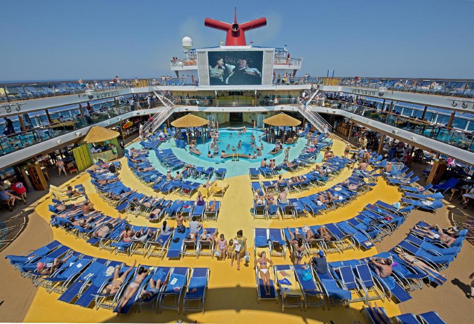In this June 23, 2012 photo provided by Carnival Cruise Lines, vacationers aboard the Carnival Breeze enjoy sunbathing at sea while viewing a movie at the Carnival’s Seaside Theatre, a lido deck poolside 270-square-foot LED screen offering concerts, sporting events and other programming throughout the day as well as nightly “Dive In Movies. (AP Photo/Carnival Cruise Lines, Andy Newman)