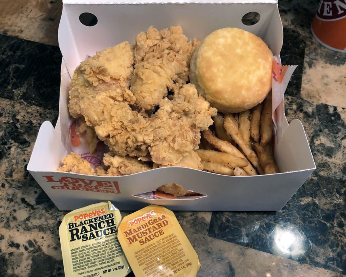 Popeyes three-piece tenders combo in the serving box with Blackened Ranch Sauce and Mardi Gras Mustard Sauce cups on a granite countertop