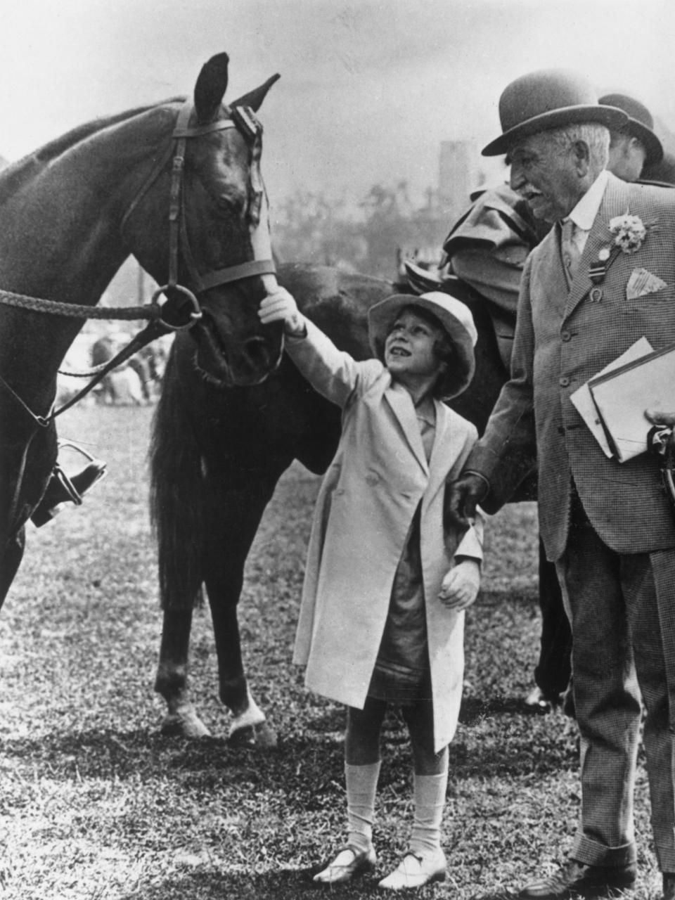 Princess Elizabeth, later Queen Elizabeth II, reaches up to pat the head of a horse at the Richmond Royal Horse Show on 6th June 1934.