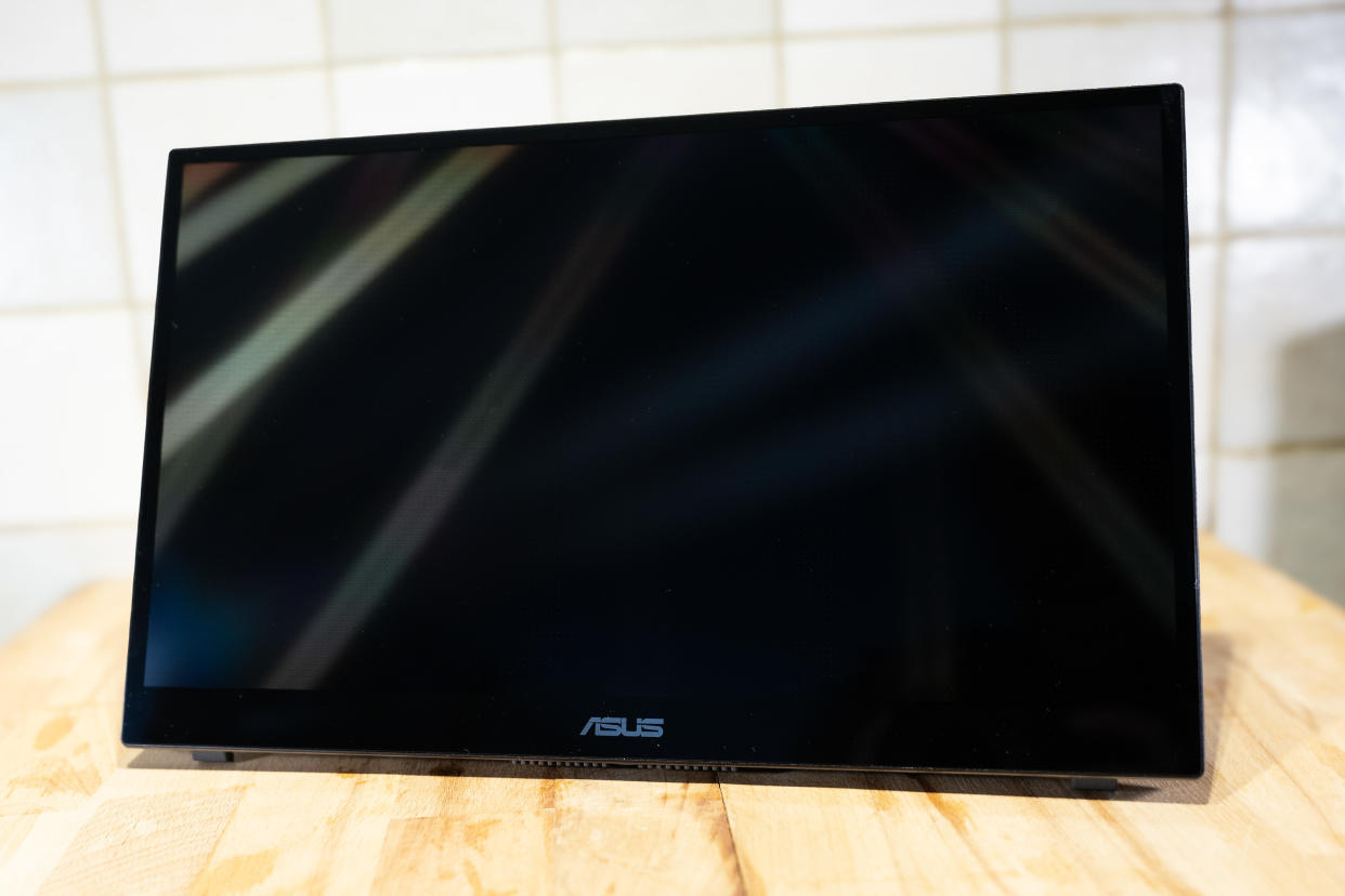  A black ASUS ZenScreen Ink MB14AHD monitor and accompanying stylus on a light wooden desk. 