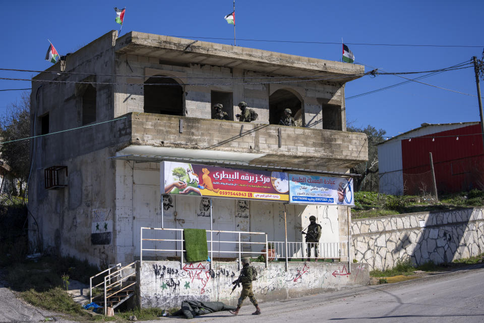 Israeli soldiers stand guard at a checkpoint near the entrance to the Palestinian village of Burqa on the road leading to the Jewish settlers Yehsiva of the West Bank outpost of Homesh, Monday, Jan. 17, 2022. Palestinian residents of Burqa say the settlers' continued presence in Homesh, which was officially dismantled in 2005, makes it difficult to access their land and move safely in and out of their village. (AP Photo/Ariel Schalit)