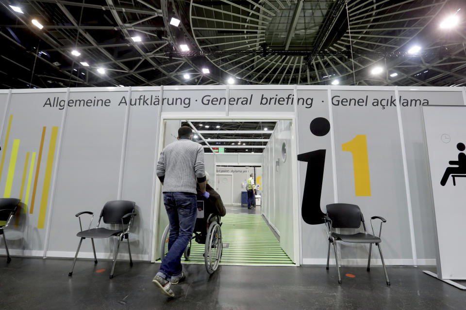 A person in a wheelchair is guided in a new coronavirus, COVID-19, vaccination center at the 'Velodrom' (velodrome-stadium) in Berlin, Germany, Wednesday, Feb. 17, 2021. (AP Photo/Michael Sohn, pool)