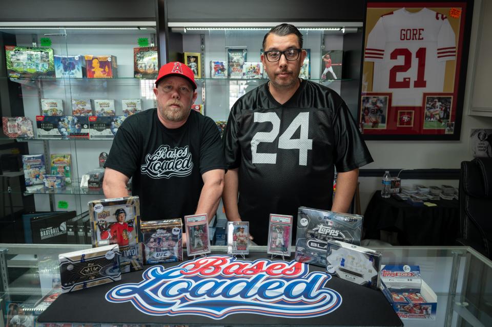 Bases Loaded business partners James Watson and Chris Bowman pose for a photograph along side some of their favorite collectibles placed on their custom rip mat on Wednesday, May 1, 2024 in Apple Valley. The shop, located at 18835 Highway 18, is stocked with cards, collectibles, and everything from individual cards worth a couple of bucks to sealed boxes to autographed jerseys and memorabilia.