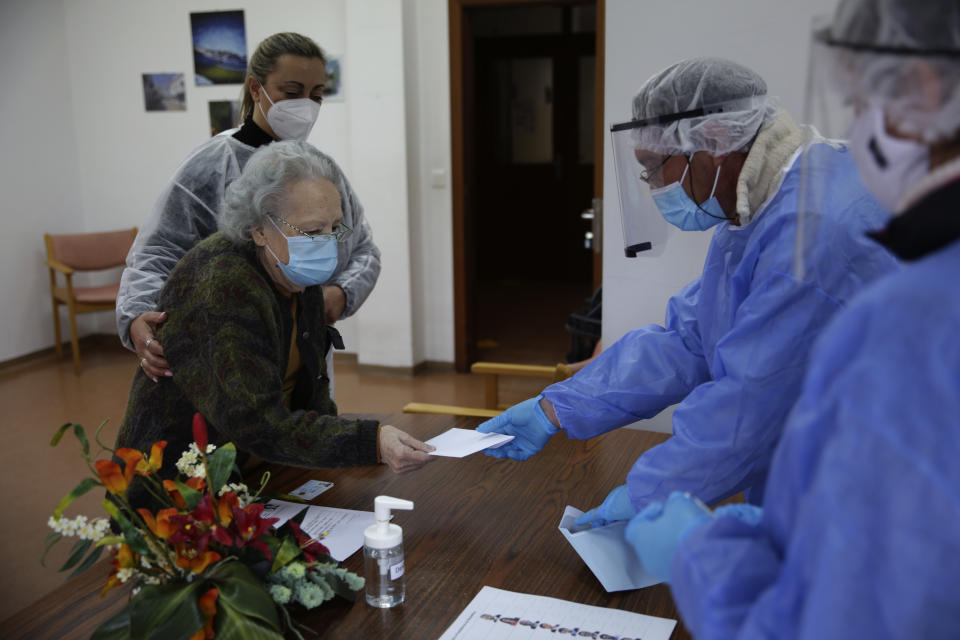 FILE - In this Tuesday, Jan. 19, 2021 file photo, Rosa Gordo, 89, hands her presidential election ballot to municipal workers in protective gear at the elderly care home where she resides in Montijo, south of Lisbon. Portugal holds a presidential election on Sunday, Jan. 24, 2021 and the moderate incumbent candidate is widely seen as the sure winner. But an intriguing question for many Portuguese is how well a brash new populist challenger fares in the ballot. Mainstream populism is a novelty in Portugal. (AP Photo/Armando Franca, File)