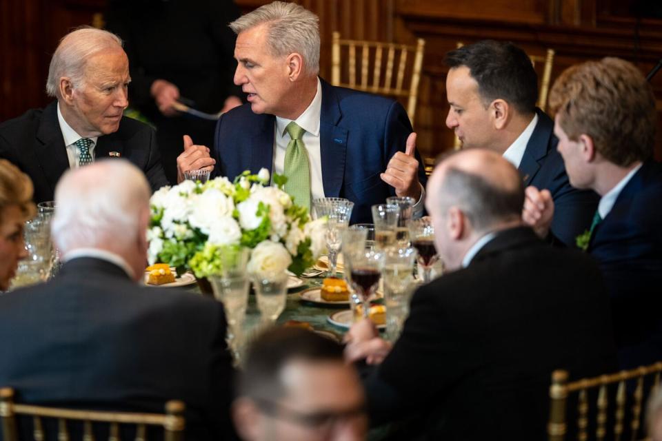 Several men in suits sit around a table and talk.