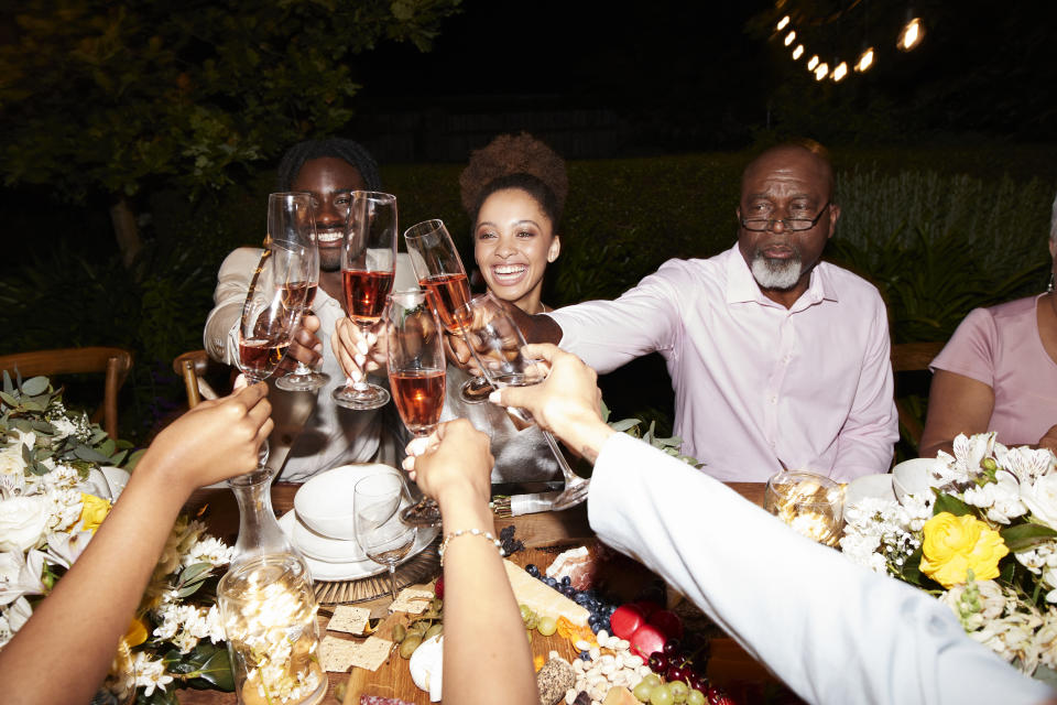 A group of people, including three identified as a woman with a curly hairstyle, a man with glasses and a beard, and another woman, clinking glasses at a dinner table