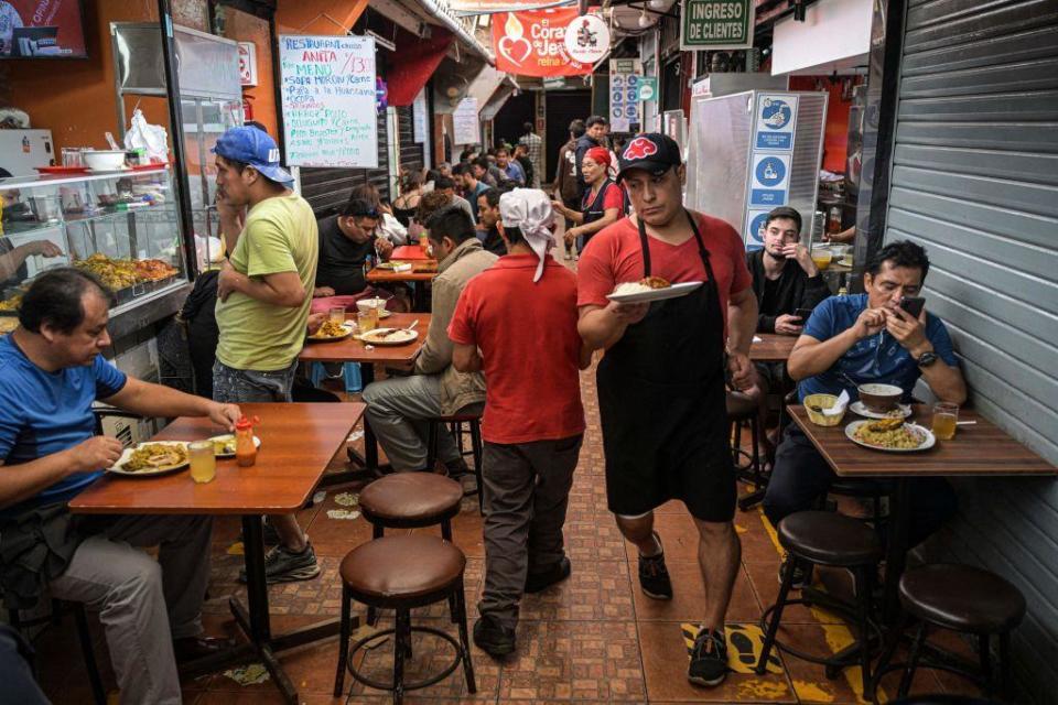 Un camarero atraviesa con un plato de comida entre las mesas de un negocio de comidas en Lima