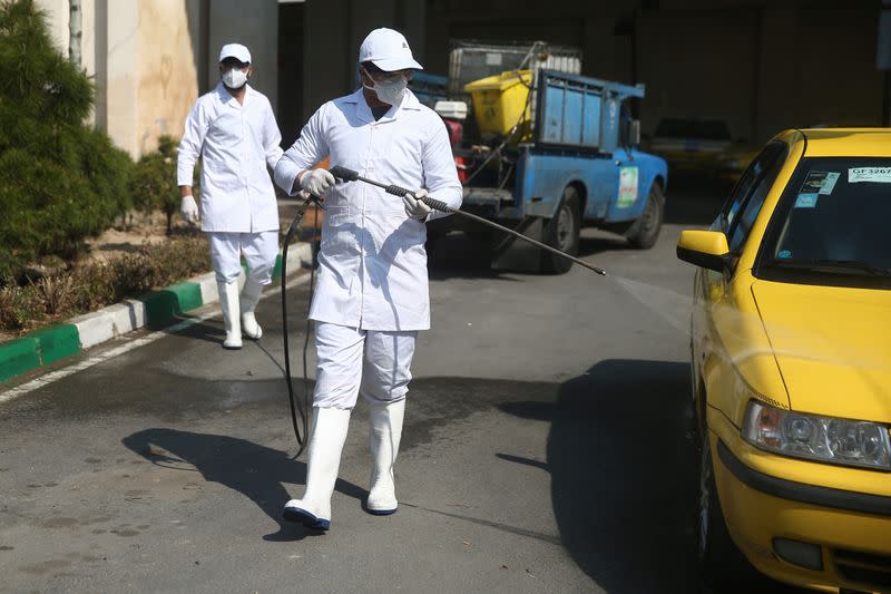 A member of the medical team wears a protective face mask, following the coronavirus outbreak, as he sprays disinfectant liquid to sanitise a taxi car in Tehran